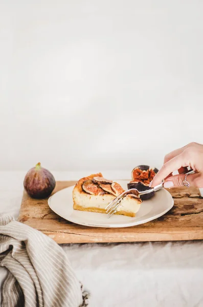 素朴な木の板の上に白い板の上に新鮮なイチジクと自家製グルテンフリーイチジクのチーズケーキを食べる女性の手 背景に白い壁 コピースペース 健康的なデザート 職人甘い食べ物のコンセプト — ストック写真