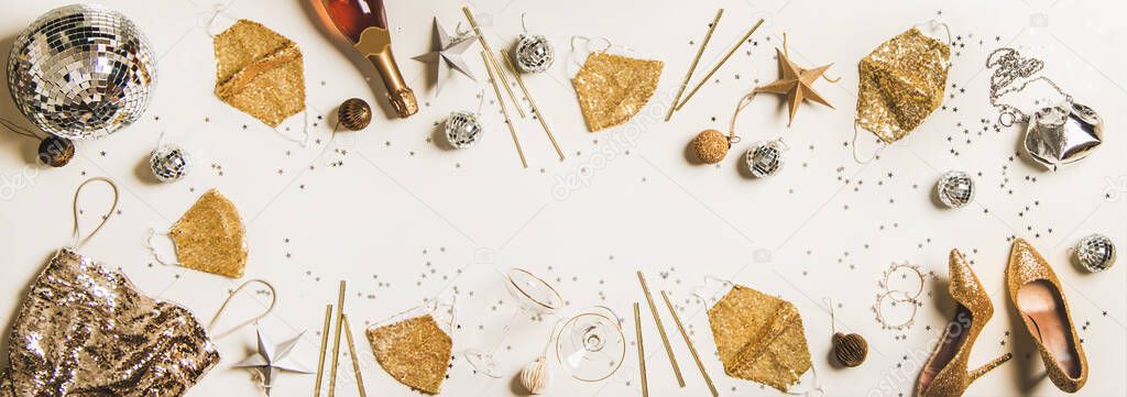Flat-lay holiday party frame with Discoball, glitter face masks, traditional golden and silver glitter decorations, shoes, dress, bag and champagne bottle over white background, top view, copy space
