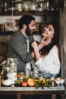Tatlı aile çiftimiz mutfakta birlikte yemek pişirirken eğleniyor. Neşeli beyaz bir adam ve yüzünde un olan esmer bir kadın sarılıyor, gülüyor ve narenciye pastası pişiriyor. Sevgililer Günü konsepti