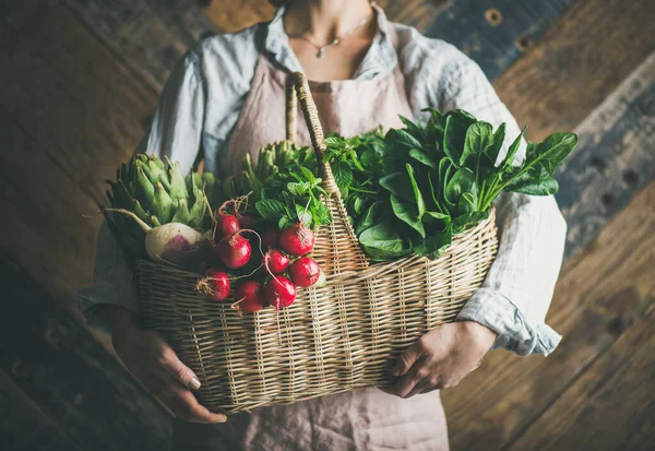 新鮮な有機庭の野菜や緑のバスケットを保持する女性農家 バックグラウンドで素朴な木製の壁 — ストック写真