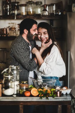 Sevgi dolu çift mutfakta birlikte yemek yaparken eğleniyor. Gülümseyen beyaz adam ve esmer güzel kadın yüzünde unla sarılıyor, gülüyor ve turunçgil pastası pişiriyorlar. Sevgililer Günü