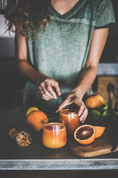 若い女性は 搾りたてのブラッドオレンジジュース またはコンクリートキッチンカウンターの近くでスムージーを作ります 健康的なライフスタイル ビーガン ベジタリアン アルカリ性ダイエットコンセプト — ストック写真
