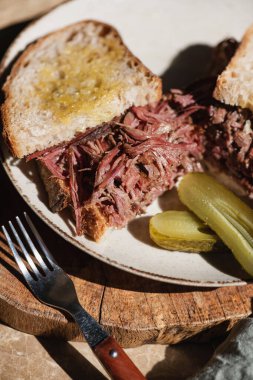 Ev yapımı sığır etli Reuben sandviçi, ekşi ekmek ve ahşap tahta üzerinde salatalık turşusu, yakın plan. Sağlıklı yemek kavramı
