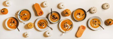 Ev yapımı balkabağı kreması çorbası tabakta ekşi krema, kabak tohumu ve ekmek kırıntılarıyla bembeyaz masa üzerinde balkabağı ile süslenmiş, üst manzara. Sağlıklı sonbahar konforlu gıda