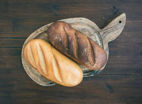 Weiße und dunkle Brotlaibe auf einem rustikalen Holzbrett — Stockfoto