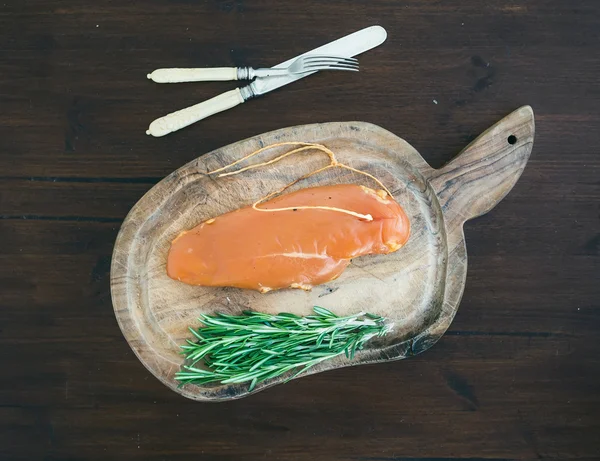 Chicken carpaccio and rosemary on a rustic wooden board over a d