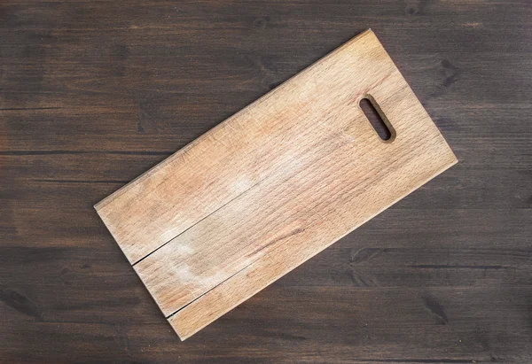 Rustic square wooden cutting board on a dark wooden desk — Stock Photo, Image