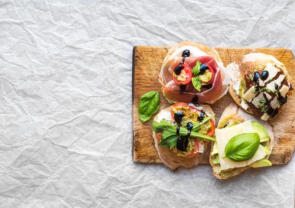 Bruschetta definido em uma tábua de madeira rústica sobre uma surfa de papel branco — Fotografia de Stock