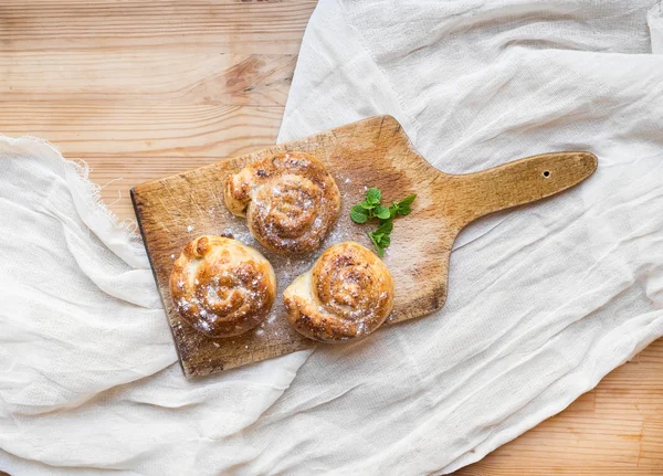 Kaneel broodjes op een rustieke houten bord over een rouwgewaad oppervlak — Stockfoto