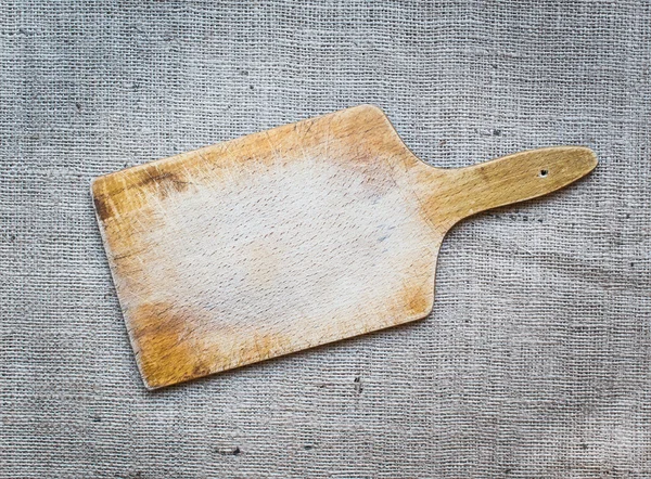 Rustic wooden cutting board over a sackcloth surface — Stock Photo, Image