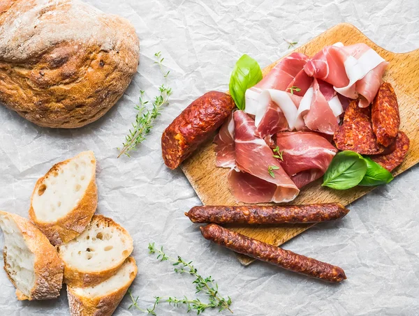 Meat appetizers selection, a loaf of rustic village bread and ba — Stock Photo, Image