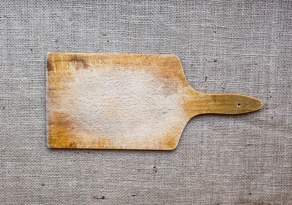 Rustic wooden cutting board over a sackcloth surface — Stock Photo, Image