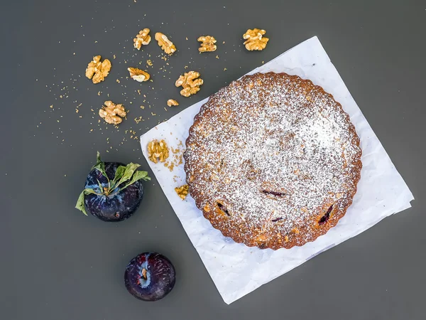 Plum cake met walnoten op wit papier op een zwarte achtergrond — Stockfoto