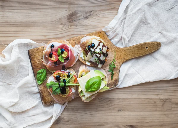 Antipasti brusquetta set on a rustic wooden board over a linen k — Stock Photo, Image