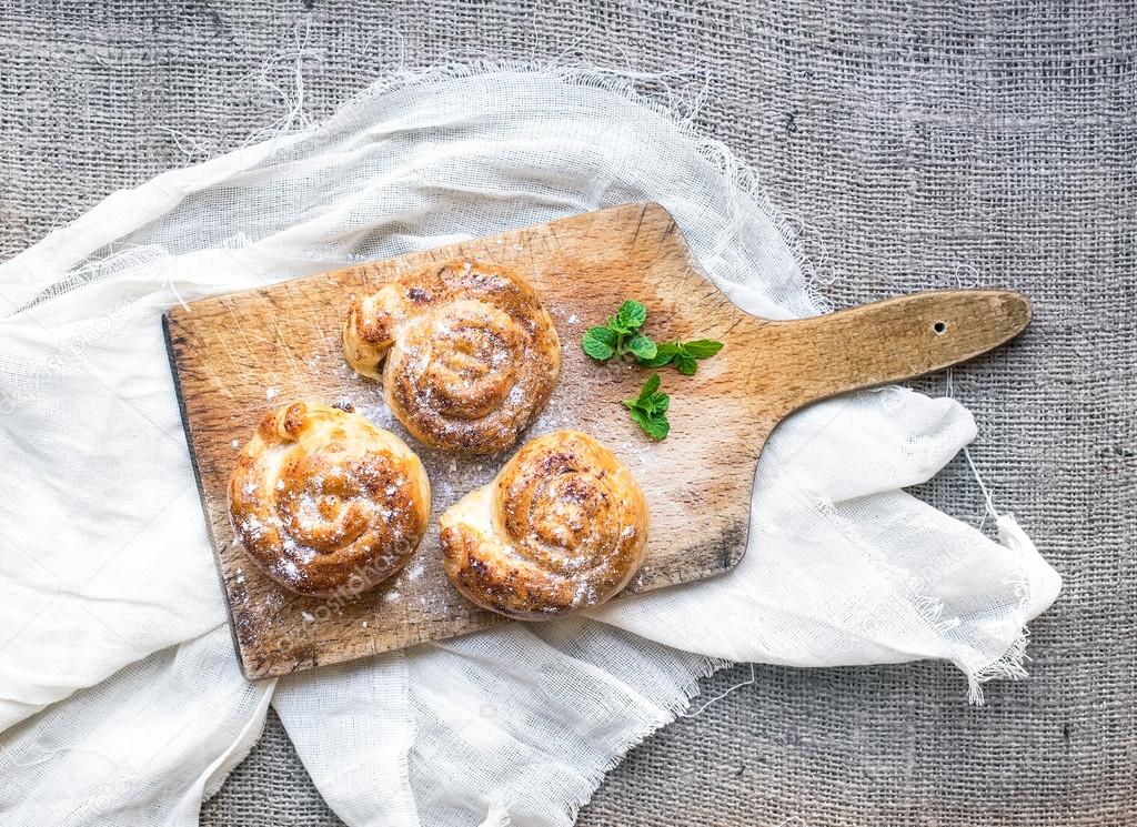 Cinnamon buns on a rustic wooden board over a sackcloth surface