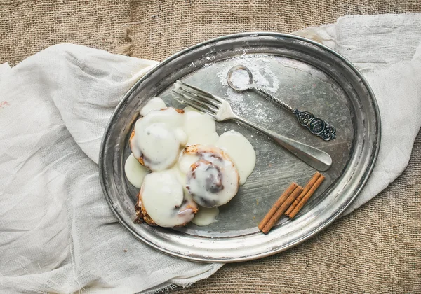 Cinnamon rolls with cream-cheese icing and cinnamon sticks on a — Stock Photo, Image