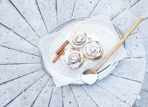 Rouleaux de cannelle avec glaçage au fromage à la crème et bâtonnets de cannelle sur un — Photo