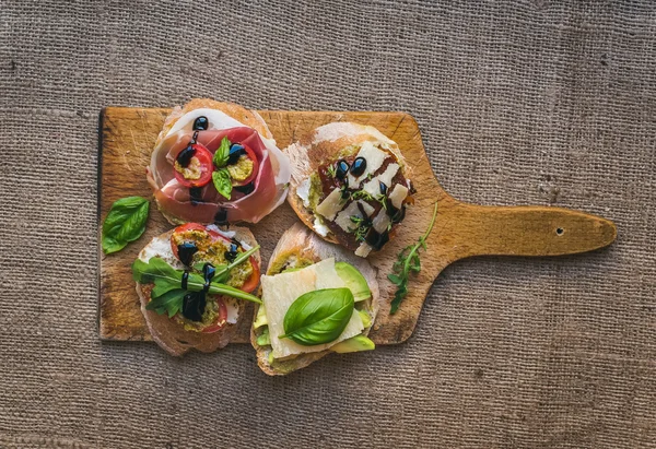 Antipasti brusquetta engastado en una tabla de madera rústica sobre un saco —  Fotos de Stock