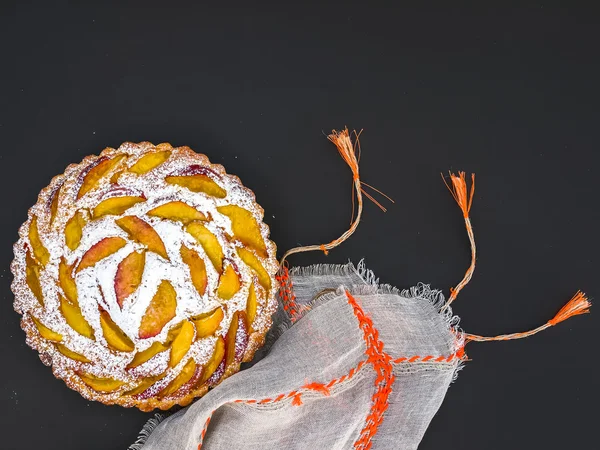 Peach pie with sugar powder over a linen table cloth on dark