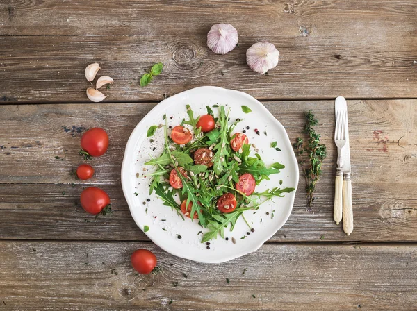 Insalata con rucola, pomodorini, semi di girasole ed erbe su fondo rustico in legno, vista dall'alto — Foto Stock