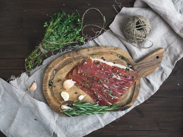 Cured pork meat or prosciutto on a rustic woodem board with garli — Stock Photo, Image