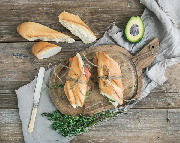 Lazac, avokádó és kakukkfű szendvicsek baguette-ben megkötött megjelöl-val dekoráció kötélen a rusztikus fa deszkán nyers fa háttér felett — Stock Fotó