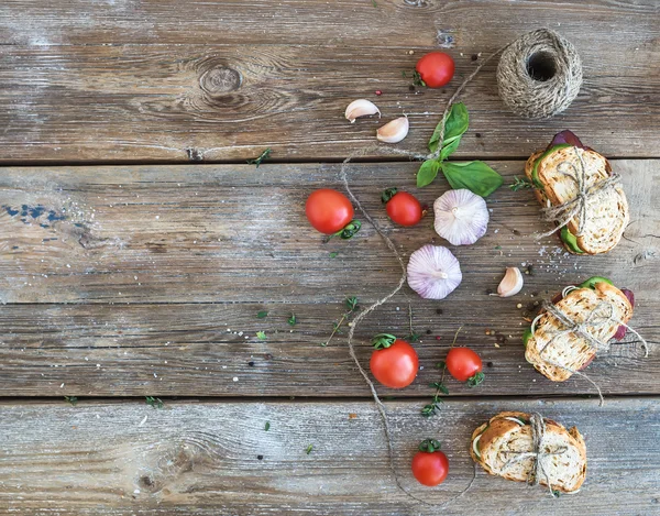 Pequeno-almoço rústico. Sanduíches com carne defumada, tomate cereja, pepino, alho, tomilho e manjericão sobre fundo de madeira áspera — Fotografia de Stock