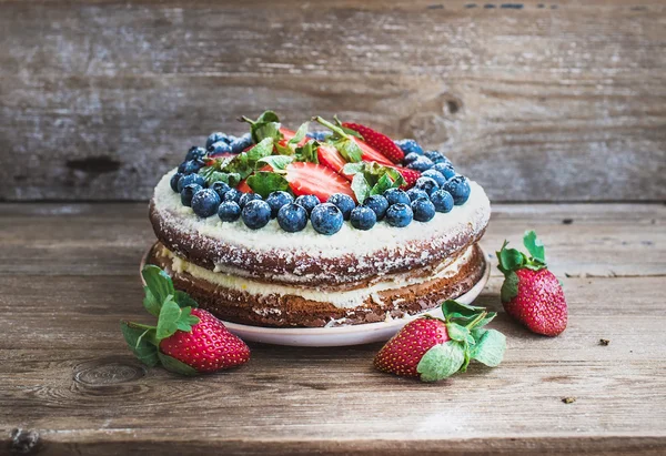 Rustic spicy ginger cake with cream-cheese filling, fresh strawberries and blueberries over a rough wood background — Stock Photo, Image