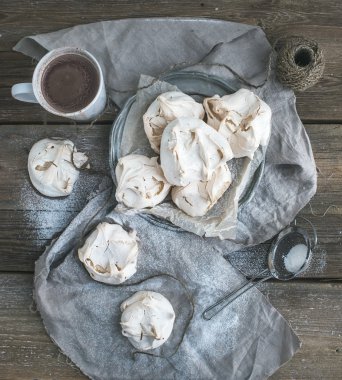 White meringue and mug of hot chocolate on a rustic wooden table. Black background, top view. clipart
