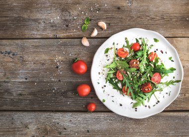 Roka, domates, Ayçekirdeği ve üstten görünüm rustik ahşap arka plan üzerinde beyaz seramik plaka üzerinde otlar ile salata