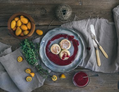 Rustik kahvaltı seti. Rus peynir kek İsveç kirazı reçel, taze kumquats, kekik, dekorasyon ip ve kaba ahşap Resepsiyon üzerinde eski yemek vintage bir metal plaka üzerinde