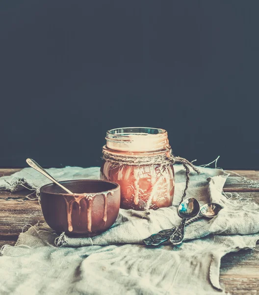 Sauce caramel salée dans un bocal en verre rustique et une tasse en céramique marron sur un bureau en bois — Photo