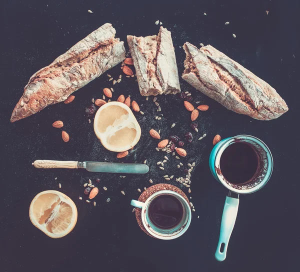 Rustikales Frühstücksset aus französischem Baguette, Grapefruit, Sonnenblumenkernen, Mandeln und Kaffee auf dunklem — Stockfoto