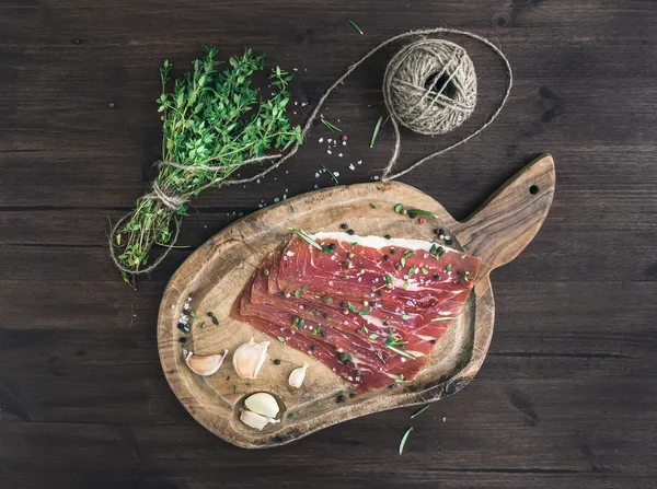 Carne de porco curada (prosciutto) em um tabuleiro rústico de woodem com alho, especiarias e tomilho — Fotografia de Stock