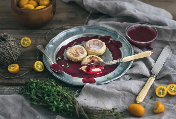 Σύνολο χωριάτικο πρωινό. Ρωσική τυρί κέικ σε ένα εκλεκτής ποιότητας μεταλλική πλάκα με lingonberry μαρμελάδα, φρέσκο κουμκουάτ, θυμάρι, διακόσμηση σχοινί και παλιό σερβίτσιο πέρα από την τραχιά ξύλινη επιφάνεια εργασίας — Φωτογραφία Αρχείου