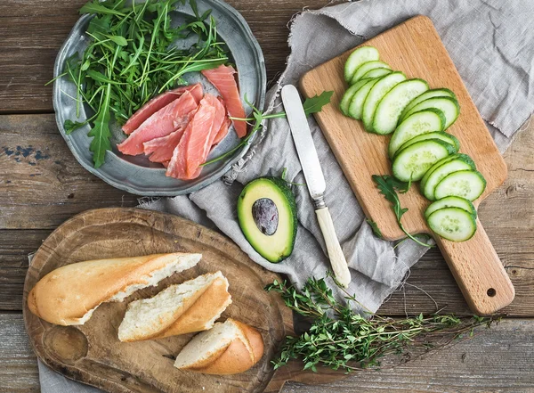 Salmon, avocado and thyme sandwiches in baguette tied up with decoration rope on a rustic wooden board over rough wood background — Stock Photo, Image