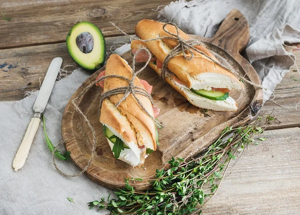 Salmon, alpukat dan thyme sandwich dalam baguette diikat dengan tali dekorasi pada papan kayu pedesaan di atas latar belakang kayu kasar — Stok Foto