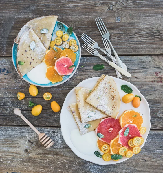 Spring vitamin breakfast set. Thin crepes or pancakes with fresh grapefruit, orange, kumquat, honey, cream and mint leaves over a rustic wood background — Stock Photo, Image