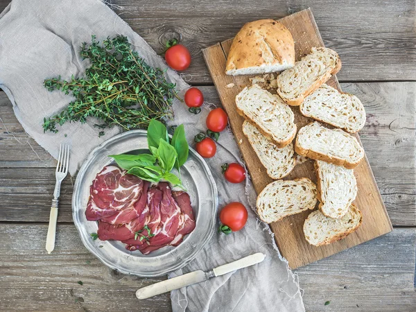 Viande fumée dans une assiette vintage argentée au basilic frais, tomates cerises et tranches de pain sur bois rustique — Photo