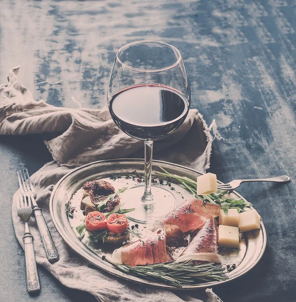 Weinvorspeise Set vorhanden. Glas Rotwein, Vintage-Geschirr, Bürste mit Kirsche, getrocknete Tomaten, Rucola, Parmesan, geräuchertes Fleisch auf silbernem Tablett über rustikaler Grunge-Oberfläche — Stockfoto