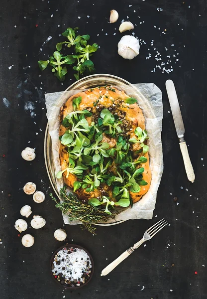 Rustic homemade pizza with fresh lambs lettuce, mushrooms and garlic over dark grunge background — Stock Photo, Image