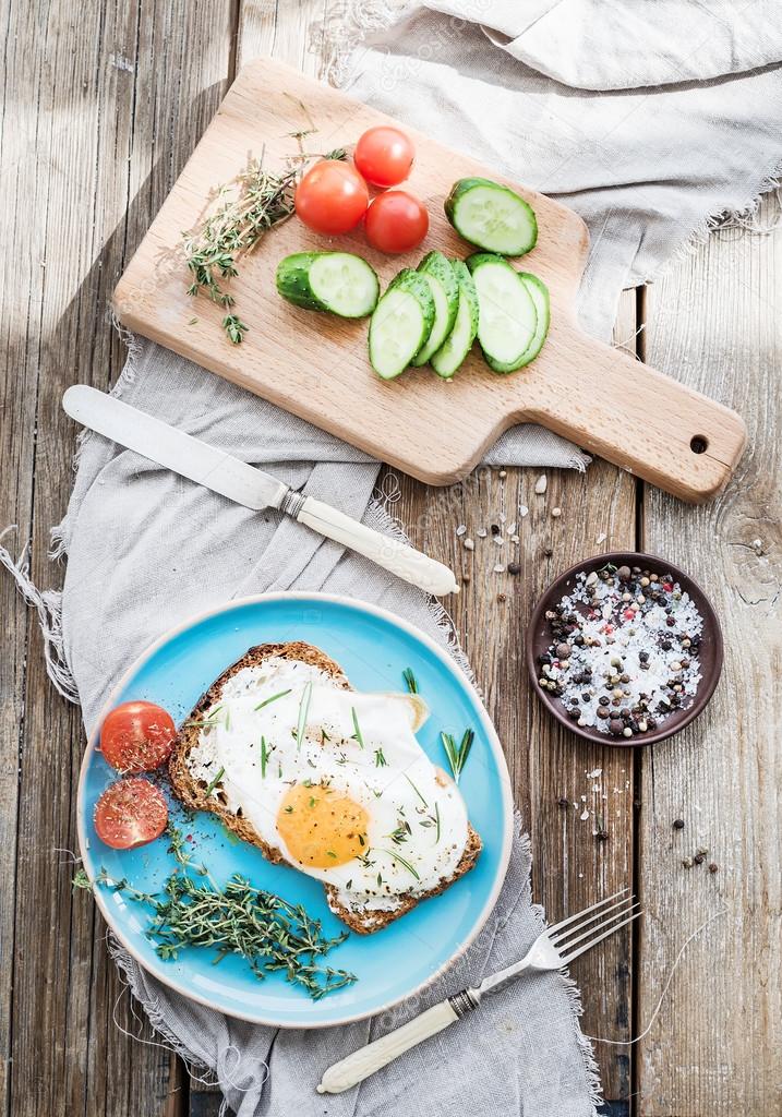 Breakfast set. Whole grain andwich with fried egg, vegetables and herbs on rustic wooden table, morning mood