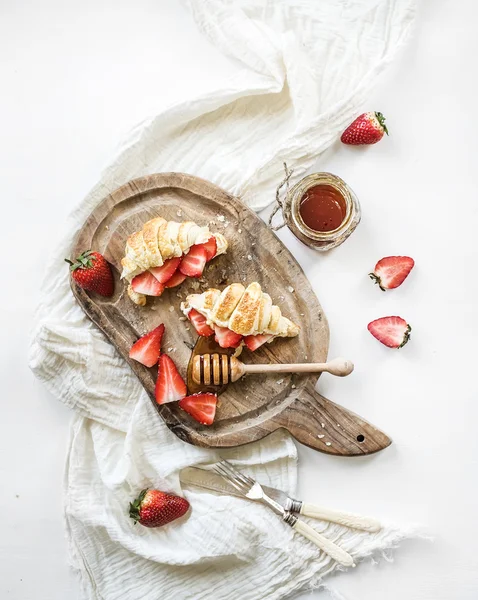 Čerstvě pečené croissanty s jahodami, mascarpone a medu na rustikální dřevěné desce nad bílé pozadí — Stock fotografie