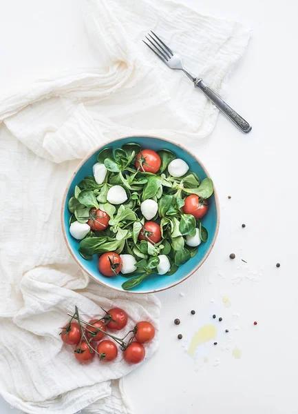 Spring salad with lambs lettuce, mozarella and cherry-tomatoes in blue ceramic bowl over white backdrop — Stock Photo, Image