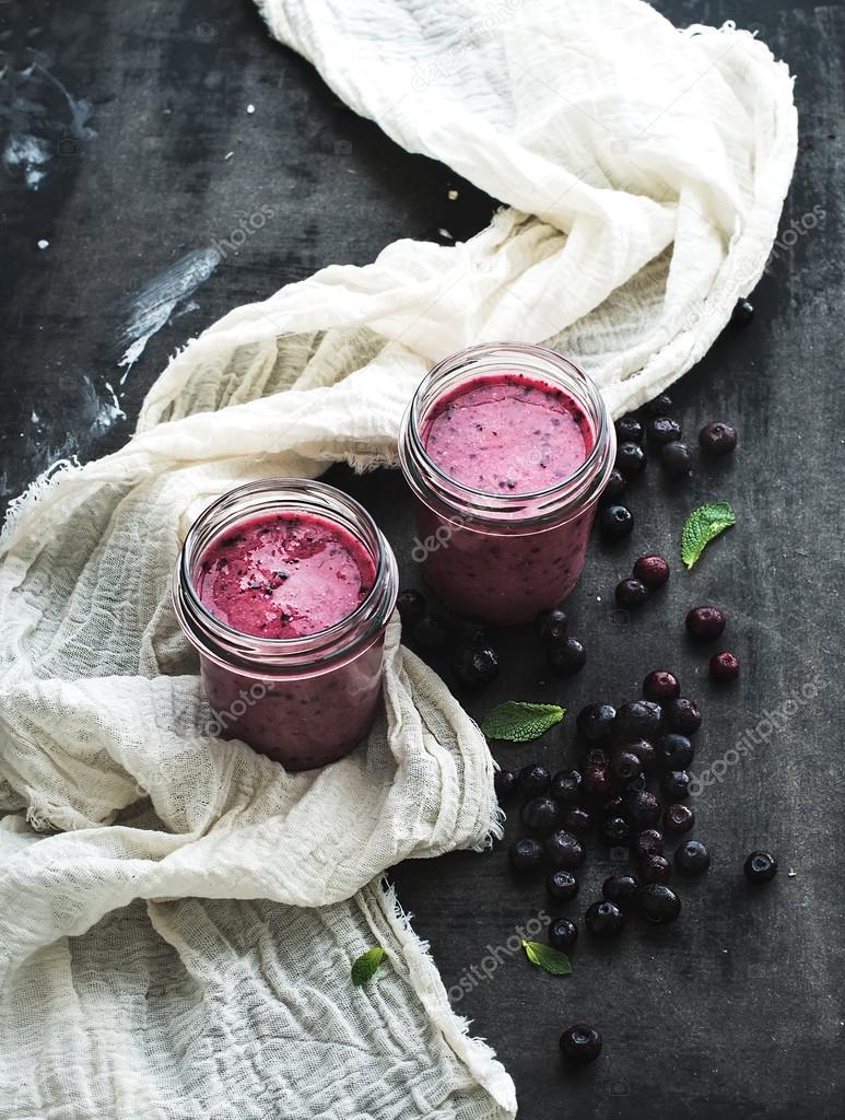 Fresh healthy smoothie in glass jars with blueberries and mint over dark grunge backdrop
