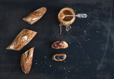 French baguette cut into pieces, sandwiches with red grapes, blueberry and salt caramel sauce on rustic dark background clipart