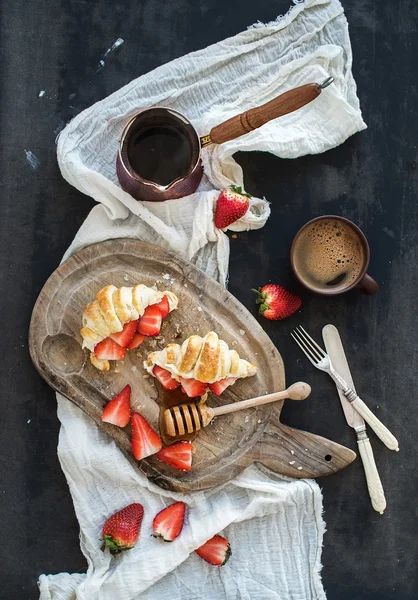 Breakfast set. Freshly baked croissants with strawberries, mascarpone, honey and coffee on rustic wooden board over dark grunge backdrop — Stock Photo, Image