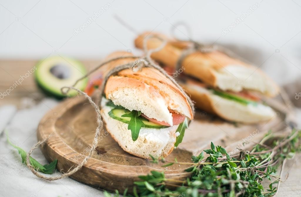 Salmon, avocado and thyme sandwiches in baguette tied up with decoration rope on a rustic wooden board over rough wood background