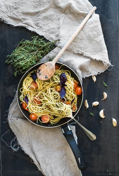 Pasta de espaguetis con salsa de pesto, albahaca, tomates cherry, ajo y tomillo en una sartén de cocción en la vieja mesa oscura grunge — Foto de Stock