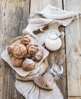 Tarçınlı çörek rustik ahşap masa, sürahi süt, karanlık grunge yüzey üzerine pudra şekeri ile